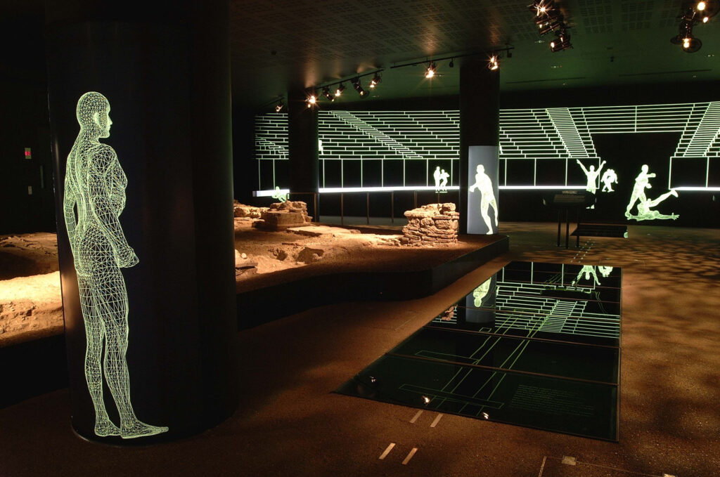 The ruins of the Roman amphitheatre in a museum setting, with 5 neon figures exercising as part of the exhibit