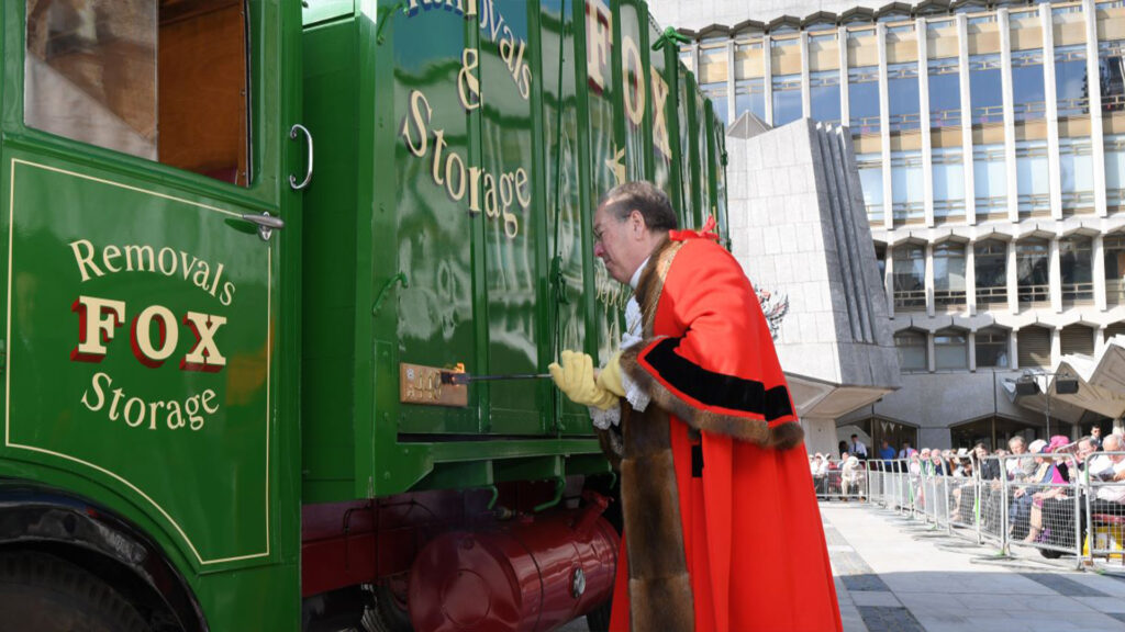 Annual Cart Marking Ceremony. A person wearing bright red robes using a red hot iron to brand a green vehicle in Guildhall Yard.