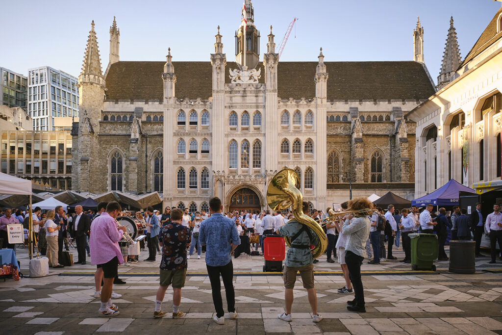 Brass band playing to a crowd with their backs to the camera, facing historic building