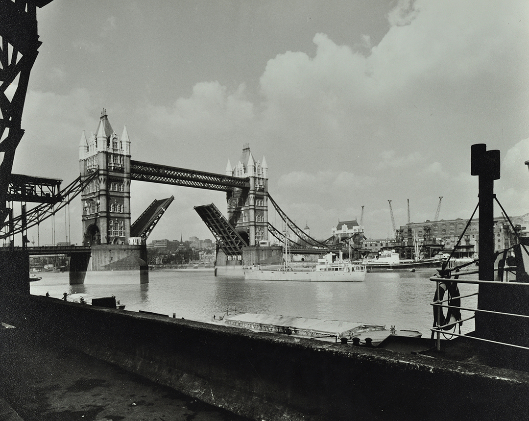 Black and white image of Tower Bridge with its bascules lifted and a boat on the river Thames about to go underneath them