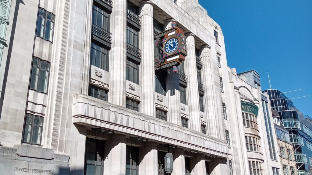 White stone building with colourful clock (Daily Telegraph building), and a glimpse of the black art deco Daily Express building.