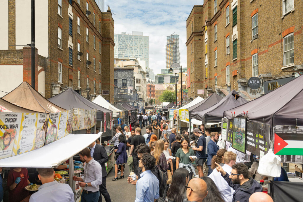 A view of Petticoat Lane, flanked by stalls on both sides, with people browsing through them.