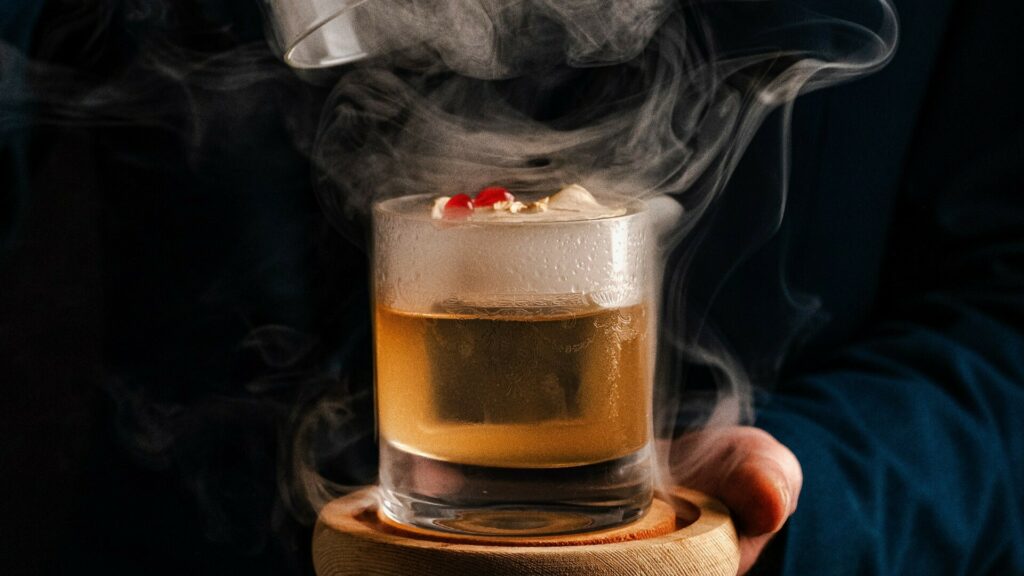 A hand holding a glass with a drink in it and steam rising.