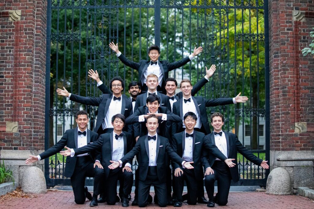 Group of people in black tuxedos with arms stretched.