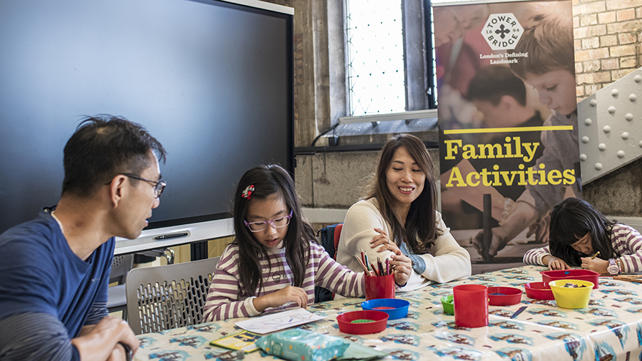 Family doing crafts in a museum. There is a banner behind that reads Family Activities with an image of Tower Bridge