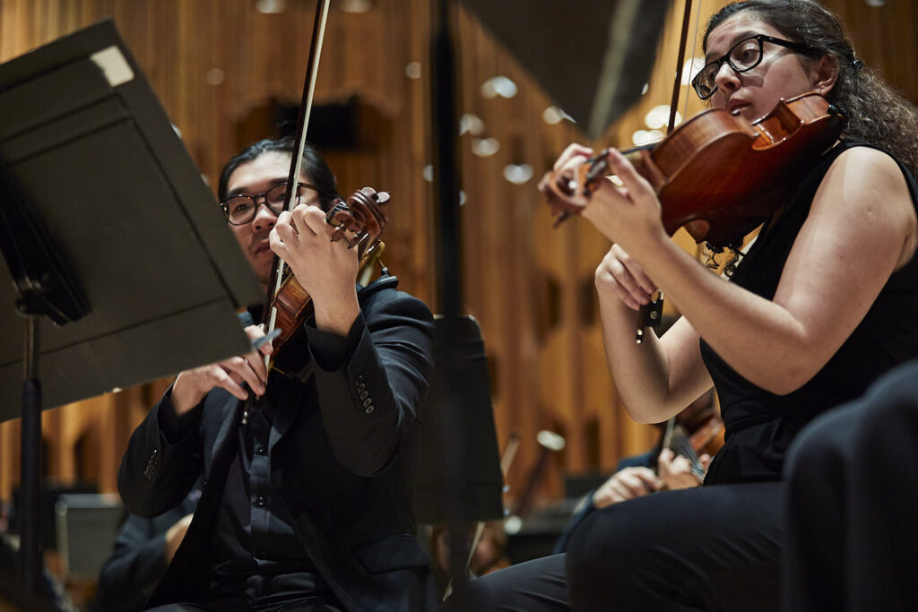 Two musicians playing their violin at a concert hall