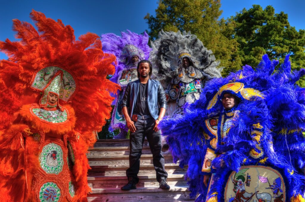 A man stands beside four people dressed up in vibrant colourful feathers,