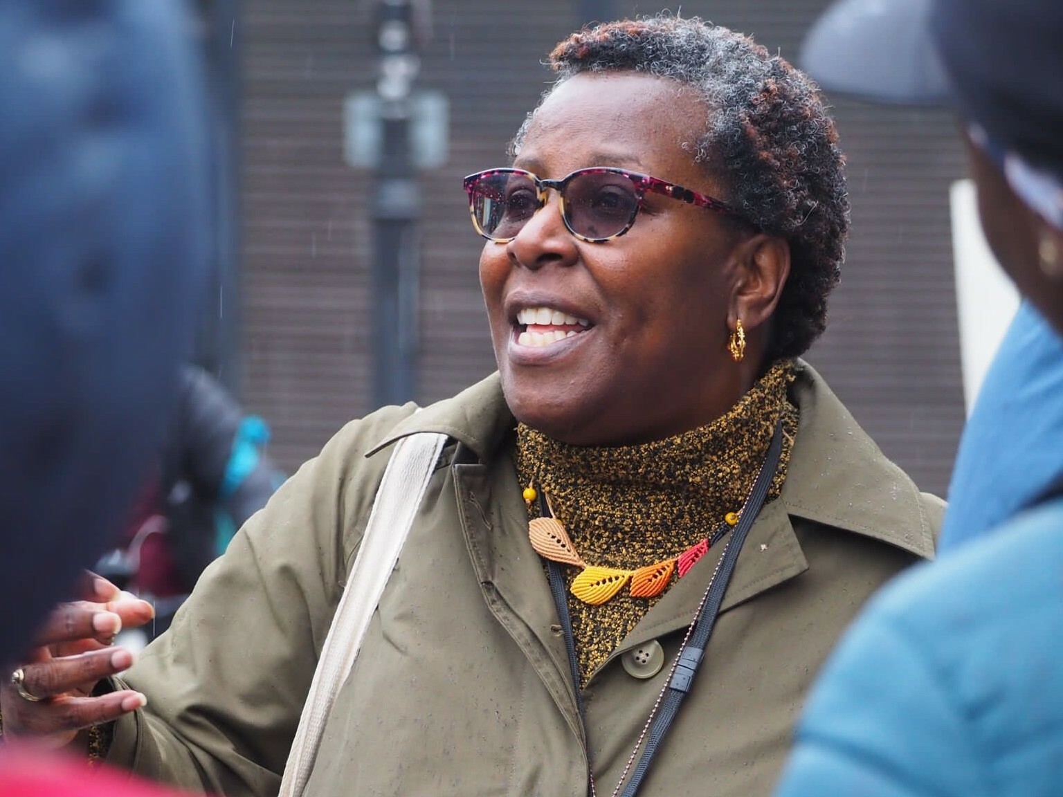 close-up shot of a woman wearing a green coat and sun glasses talking to a group of people