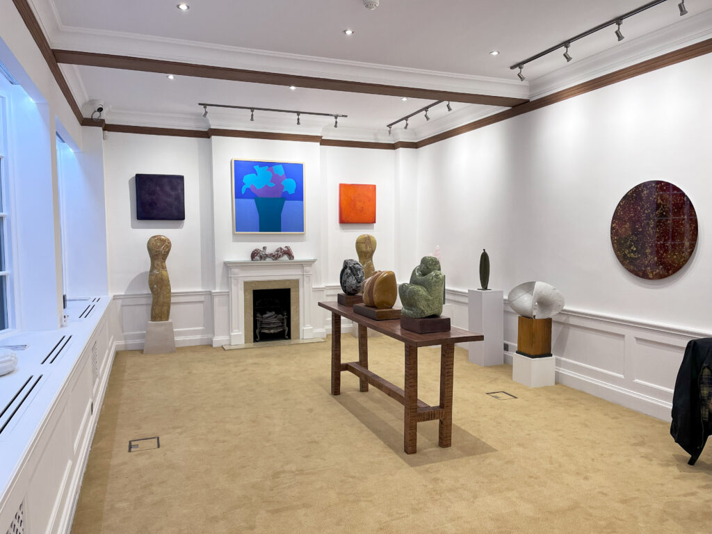 Interior of Crane Court Gallery featuring diverse artworks, including sculptures on pedestals and colourful paintings on the walls. The room has a neutral colour scheme with elegant architectural details.