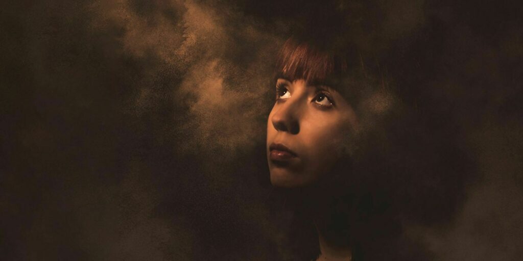 Profile of a person with short hair against a textured, dark brown background, with a contemplative expression.