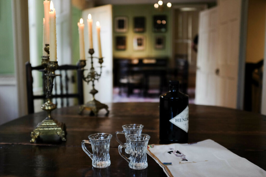 A cozy dining setting with a bottle of Hendrick's on a table flanked by two glasses and candlesticks, in a room with soft lighting and muted colors.