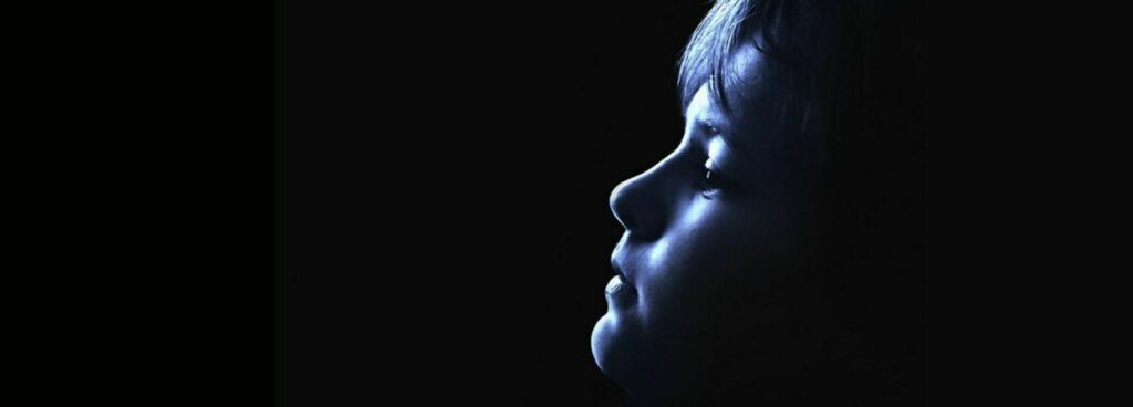 Close-up profile silhouette of a child lit in blue light against a dark background.