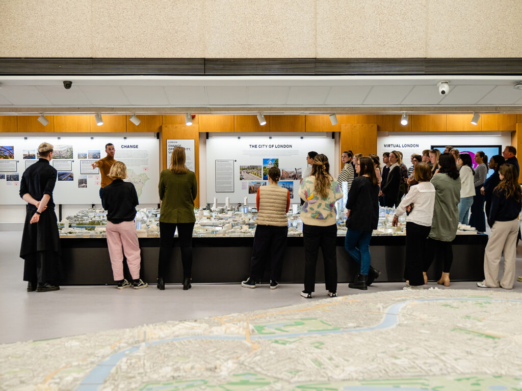 A group of people standing around a large model of London listening to a person giving a talk.